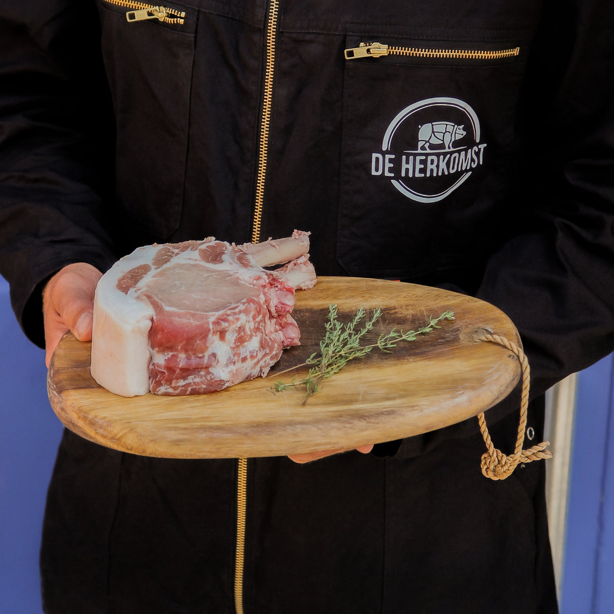 Rauwe varkensribben op een houten plank, vastgehouden door een medewerker van De Herkomst